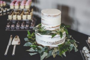 Naked cake surrounded by greenery and cupcakes.