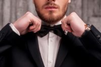 A man in a tuxedo adjusting his bow tie.